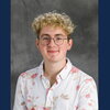 A man in a pink and white shirt with curly blonde hair and glasses.