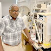 A man in a plaid shirt and glasses standing in a laboratory.