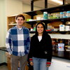 A man in a blue checkered shirt and a woman in a navy sweater stand in front of a lab bench.