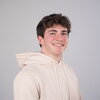 Man in cream hooded sweatshirt poses for headshot in front of grey background