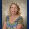 blond woman in green and blue shirt sits in front of beige backdrop