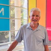 Man in blue polo stands in lab atrium with colorful signs in background