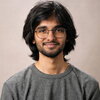 Man with black hair and glasses and beard wearing grey T-shirt