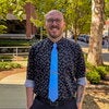 Man with glasses and short beard stands in front of tree outside Burrill Hall
