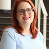 Woman with shoulder length red hair and eyeglasses wears light blue sweater