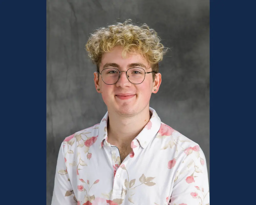 A man in a pink and white shirt with curly blonde hair and glasses.