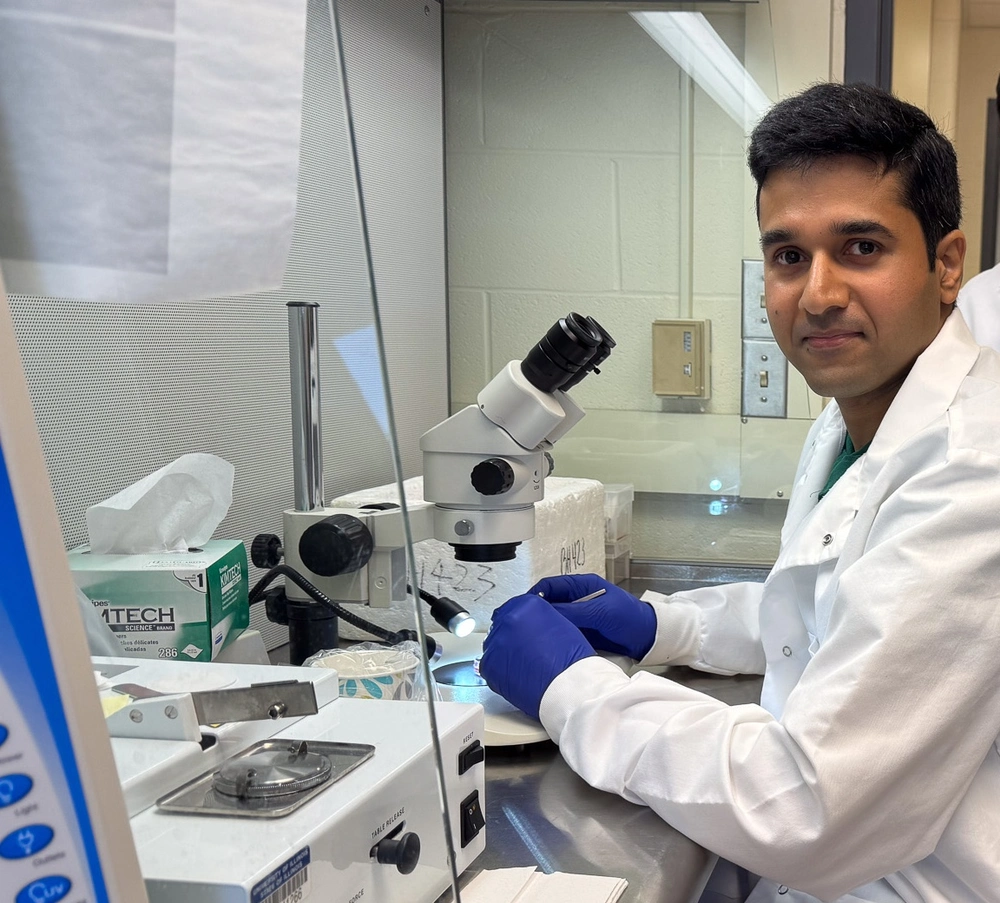 man in labcoat sits in front of a microscope