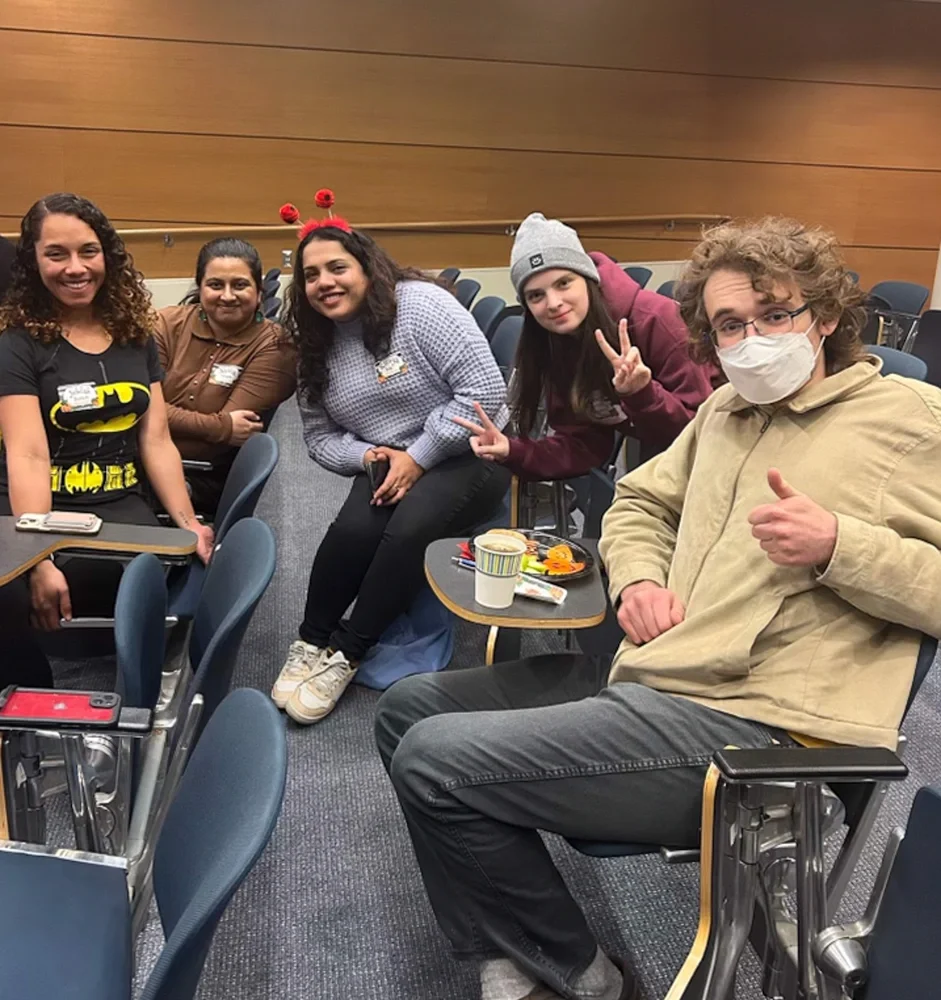 graduate students and their peer mentors give thumbs up and peace signs to camera while sitting in an auditorium