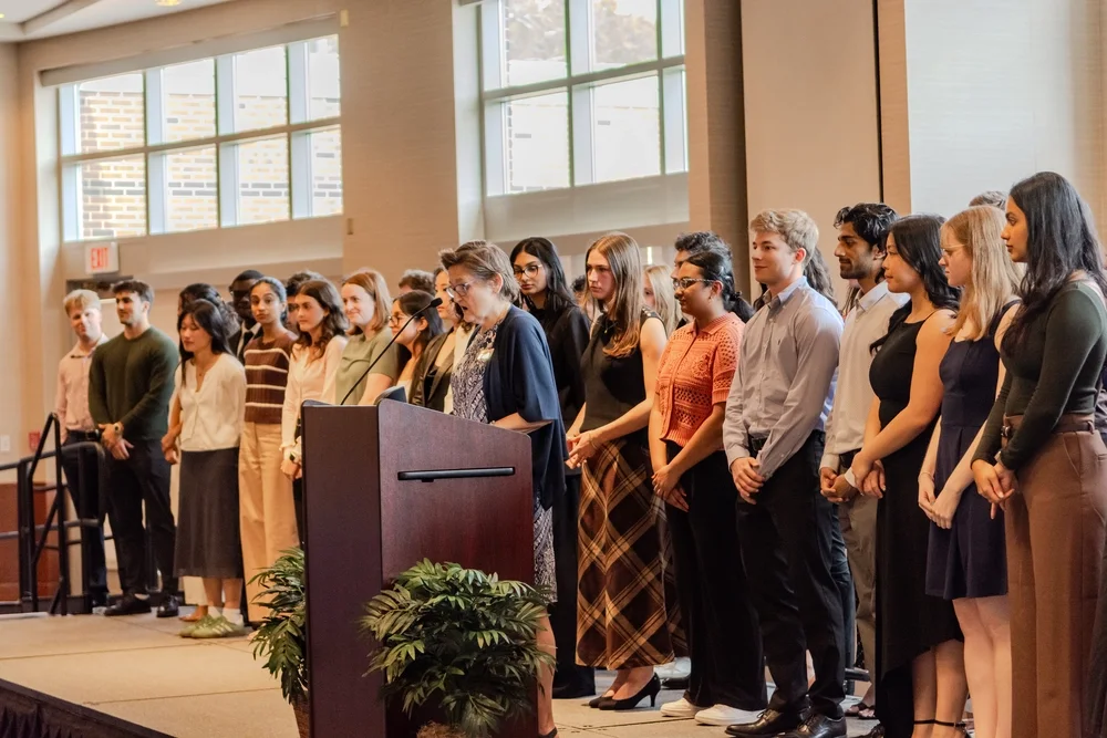 students stand on stage while being recognized for their academic achievements