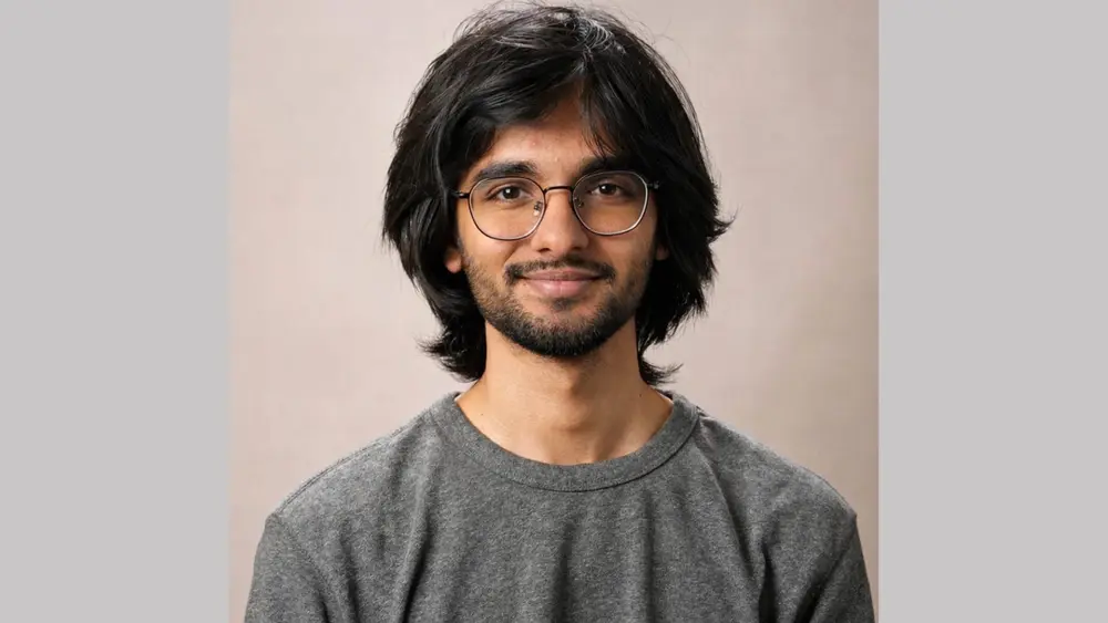 Man with black hair and glasses and beard wearing grey T-shirt