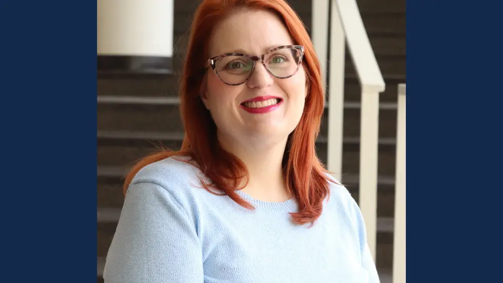 Woman with shoulder length red hair and eyeglasses wears light blue sweater