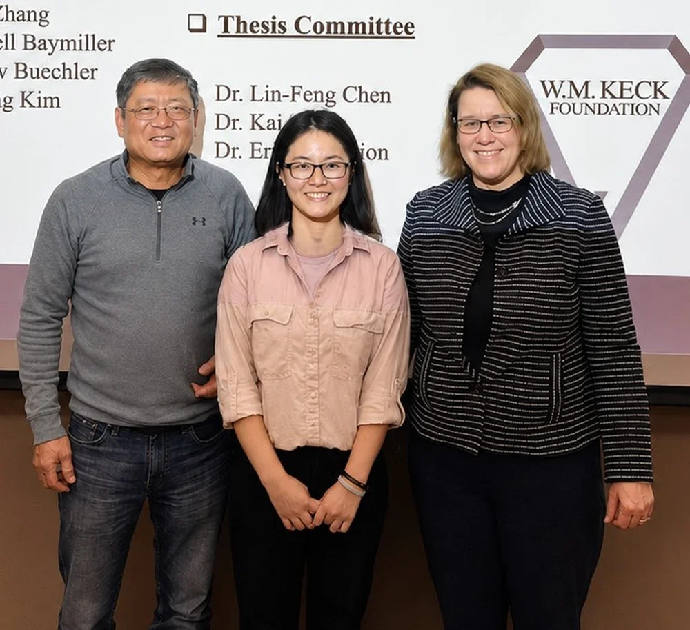 Lin-Feng Chen and Susan Martinis stand in front of projector screen with Phd student Xiaodan Lin