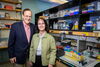 John Katzenellenbogen, left, Benita Katzenellenbogen, right, stand together in front of a lab bench, smiling for the camera. 