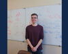 A man in a red shirt and glasses standing in front of a whiteboard.