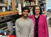 A woman in a pink blazer and a man in a grey sweater stand in a laboratory.