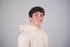 Man in cream colored sweatshirt poses for headshot in front of gray background