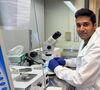 man in labcoat sits in front of a microscope