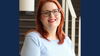Woman with shoulder length red hair and eyeglasses wears light blue sweater