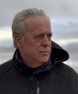 Man wears black jacket and looks to his left while outside under a cloudy sky