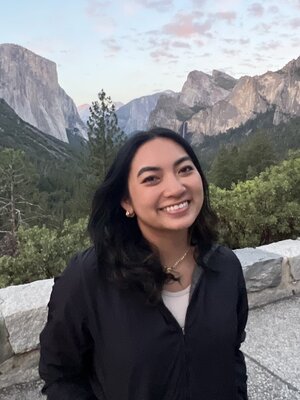 Angela Cabrera smiles for the camera outside with mountains and forest trees in the background.