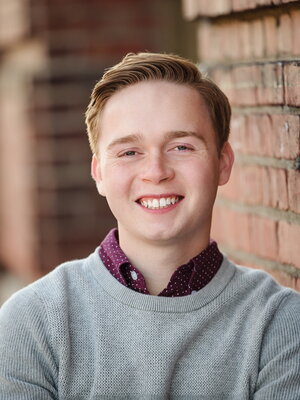 Edward Andrews smiles for the camera leaning against a brick wall. 